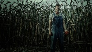 A farmer stands in a corn field gripping a bloody human heart